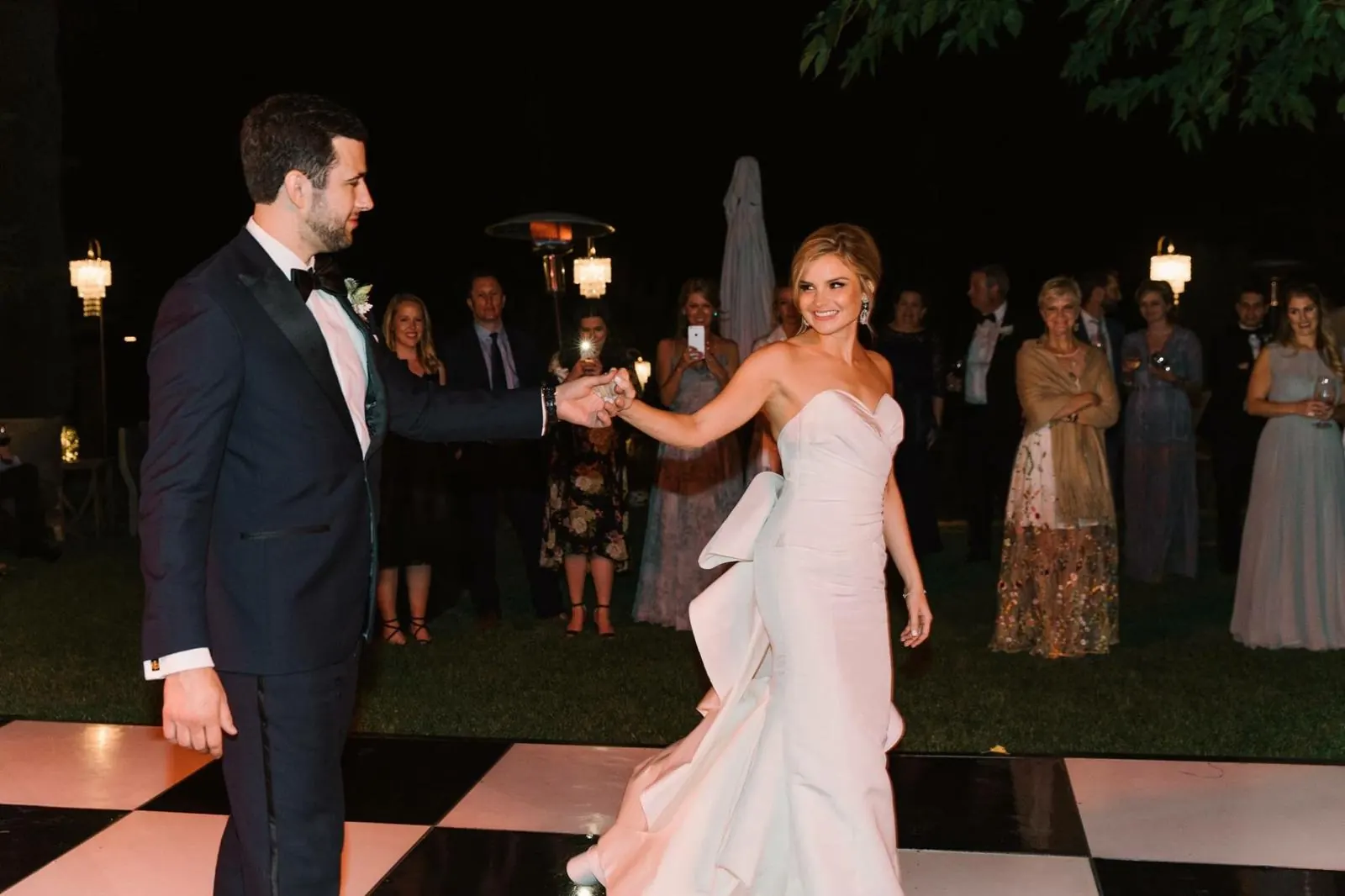 Couple holding hands open on a checkered dance floor while guests watch