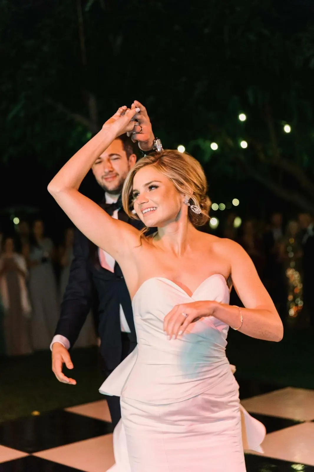 Bride smiling under the groom’s arm during their outdoor first dance