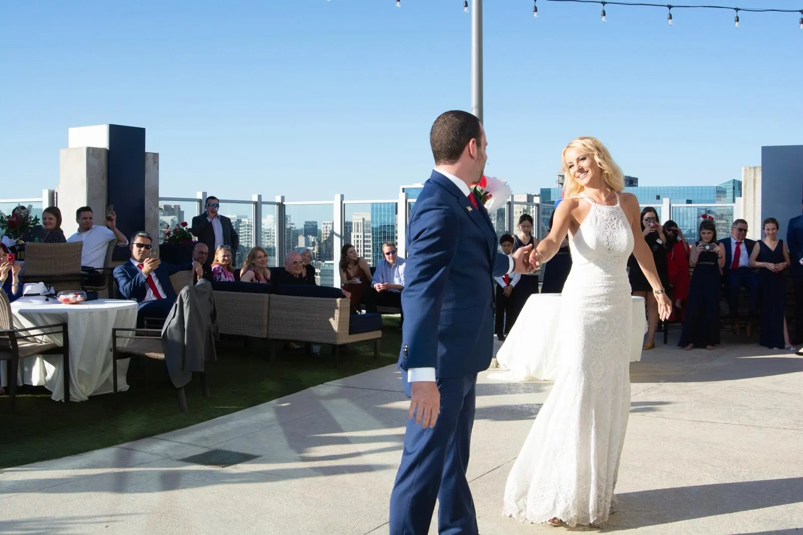 Couple dancing on a rooftop terrace with skyline and guests behind them